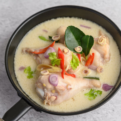 Chicken soup in a pan with cilantro, basil and peppers