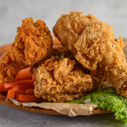 Deep fried chicken resting on a plate with carrots and lettuce