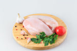 Two pieces of chicken breast on a white background and on a wooden board with tomatoes and other ingredients 